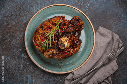 Delicious roasted ham or pork knuckle with glazed brown crispy skin, red pepper berries and rosemary on big ceramic plate on rustic stone background top view, traditional and festive family meal 