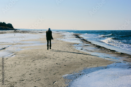 Zimowy spacer brzegiem Bałtyku. Chłodna tonacja, pomarszczona powierzchnia piaszczystej plaży, faktura, abstrakcja, tło. Biegnąca dziewczyna unosi się nad ziemią.