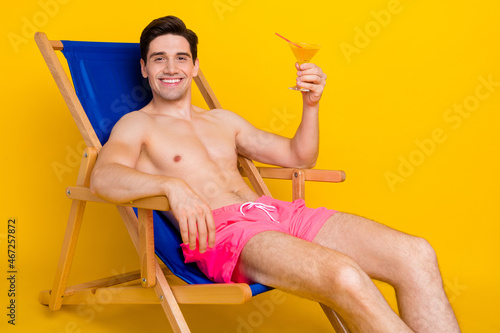 Profile side photo of young man happy positive smile sit chair drink cocktail vacation isolated over yellow color background