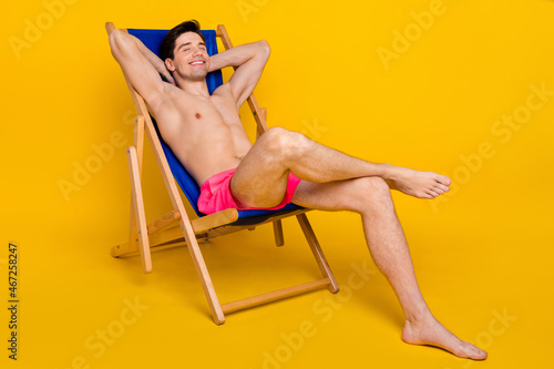 Full size profile side photo of young man happy smile sit chair relax dream hands behind head isolated over yellow color background