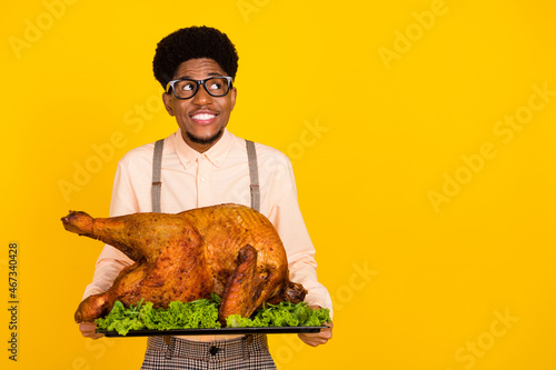 Photo of cheerful guy hold dish baked turkey look empty space wear specs suspenders shirt isolated yellow color background