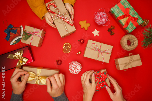 A family of three, mom, dad and child, pack Christmas gifts in craft paper and tie beautiful bows with their own hands