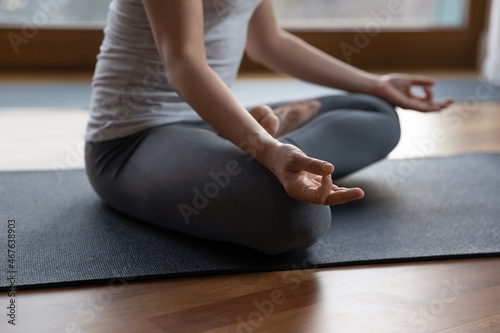 Close up cropped image young slim woman wear grey sportswear meditating sit cross-legged on mat. Stress relief, renew energy after yoga practice, sport training, mindfulness, healthy lifestyle concept