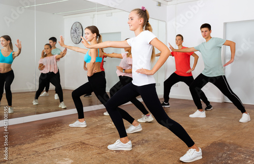Cheerful teens practicing dance, stretching with young female trainer in dance hall..