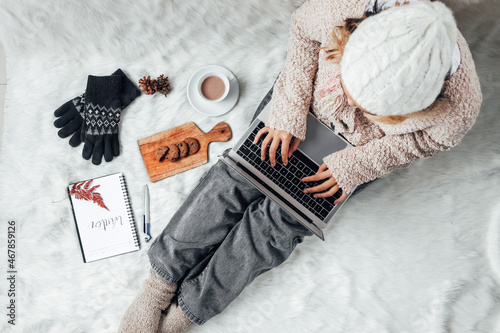 A girl with winter clothes working with laptop at home and enjoying winter season with hot chocolate and cookies