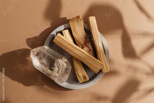 Natural crystal and Palo Santo sticks on a concrete plate, beautifully illuminated by sunlight. A set of incense for fumigation. Top view. Organic sacred tree incense from Latin America.