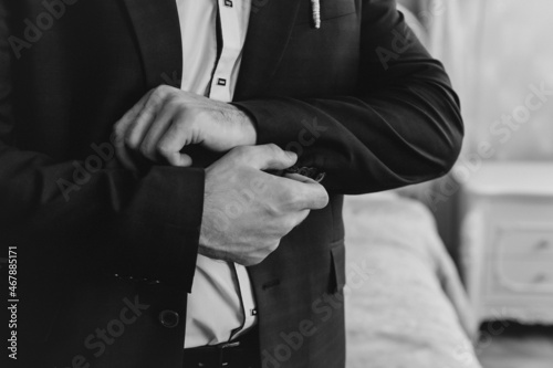 Closeup of a groom in maroon suit correcting a sleeve.