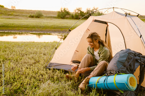 White woman tying her shoelaces while sitting in tent during camping