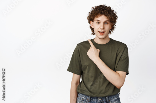 Image of young curly man pointing upper left corner, looking curious, asking question about sale banner, showing interesting advertisement, white background