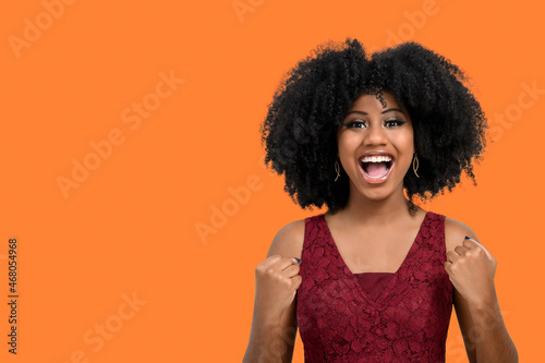A cheerful and happy young girl with afro hair proves to be the winner, raises her clenched fists in celebration. A beautiful dark-skinned girl overflows with joy or happiness,