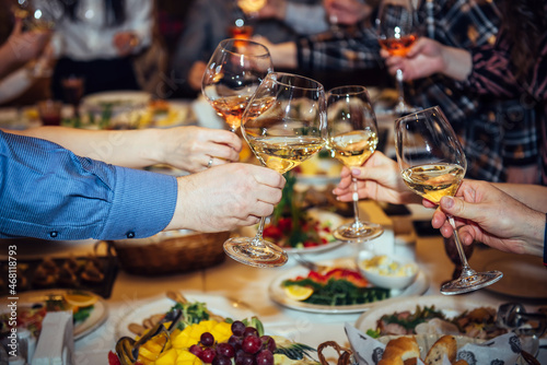 Toast at the festive table. Hands holding glasses with alcoholic beverages, close-up. Relatives and friends clinking wineglasses.