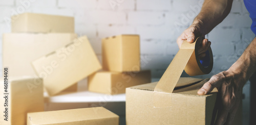 warehouse order picker packing and sealing cardboard box with tape for dispatch