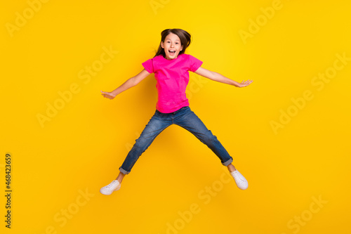 Photo of crazy active cheerful girl jump open mouth wear pink t-shirt jeans sneakers isolated yellow color background
