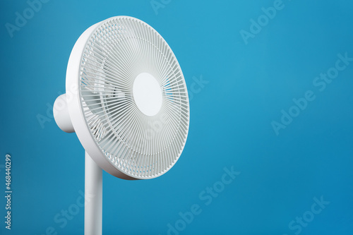 White modern electric fan for cooling the room on a blue background.