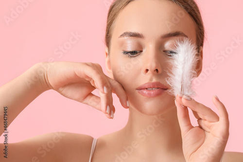 Beautiful young woman with soft feather on color background