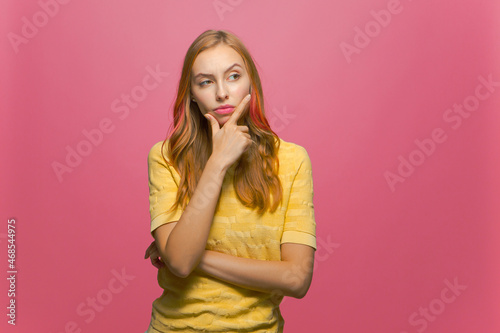 Young girl raised brow rubbing chin scheme plan thinking, pondering answer on pink studio background with copyspace