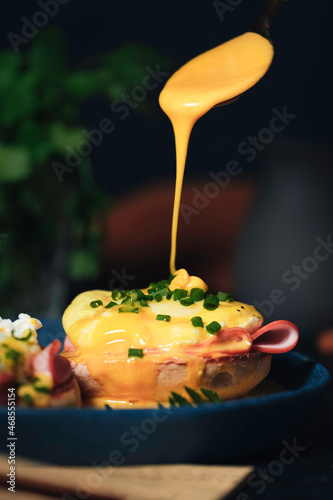 egg Benedict with hollandaise sauce on dark blue plate on table in kitchen