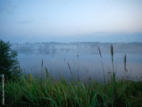 misty morning by the lake with calm water, fog and reflections of trees in mirror