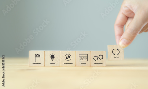 Agile development methodology concept. Flexible developing process of business growth. Agile life cycle. Hand hold the wooden cubes with agile process cycle symbols on grey background and copy space.