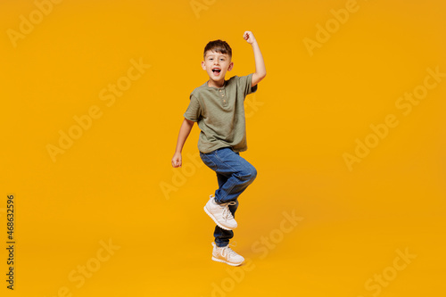 Full body little small fun happy boy 6-7 years old wearing green t-shirt do winner gesture clench fist isolated on plain yellow background studio portrait. Mother's Day love family lifestyle concept.
