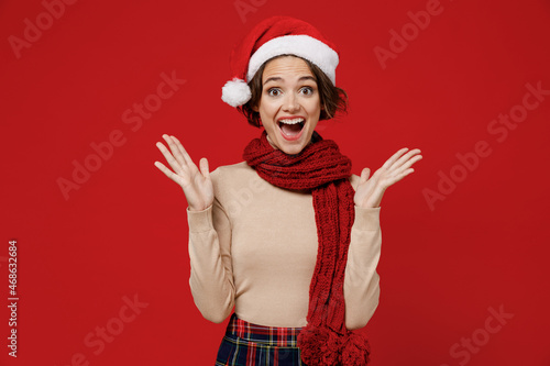 Young surprised amazed impressed shocked caucasian woman 20s wear Santa Claus Christmas red hat spread hands isolated on plain red background studio portrait. Happy New Year 2022 celebration concept.