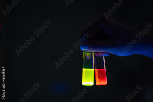 A woman researcher holding chemistry photochemical reaction glass vials in a organic laboratory - radioactive - fluorescence. A copy space black background.