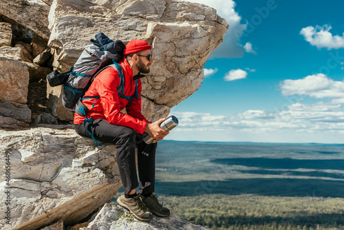 A male tourist is resting after a hard climb up the mountain. A traveler among the Rocky Mountains. A man is a traveler with a backpack among the rocks. Backpacking in the mountains. Copy space