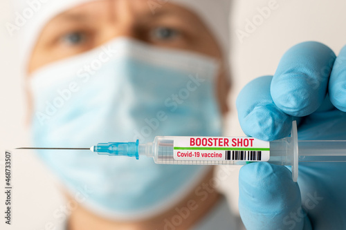 Doctor holding syringe with Covid-19 vaccine with inscription booster shot. Concept of third booster dose of vaccine