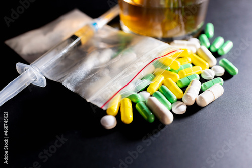 Hard drugs and alcohol on dark gray table. Alcohol pills syringe plastic bag powder of cocaine on table with shadow.Closeup.Copy space.