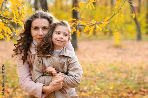 Portrait of a mother and daughter in an autumn park. Happy people pose against the background of beautiful yellow trees. They hug and are happy together.