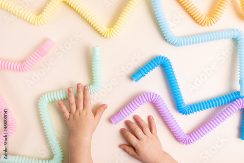 Trendy kids toys pastel colorful pop-tube in baby toddler hands on beige background. Set of forms and colors corrugated pipe and anti stressing, relaxation fidget finger toys. 