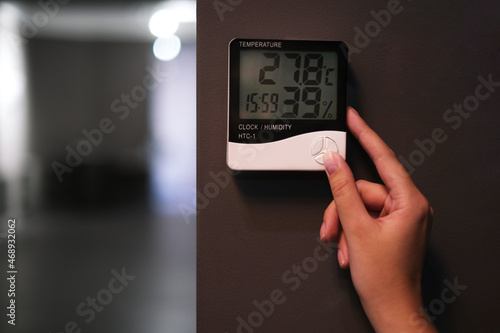 woman adjusts the psychrometer at home. device for measuring humidity and temperature on a dark wall close-up 