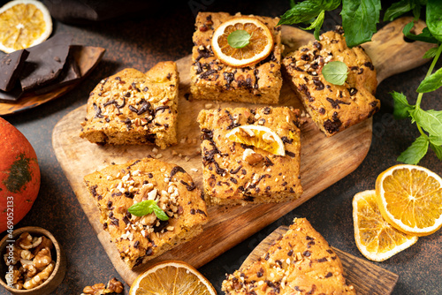 Pumpkin blondie bars with chocolate and walnuts close-up. Brownie pie slices on a serving wooden board on the dark culinary background. Baking for Thanksgiving