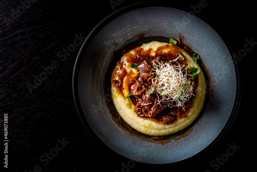 Stewed veal cheeks with mashed potatoes on plate on rustic wooden table dark background