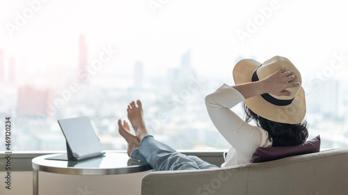 Work-Life balance and life quality concept with business woman rear view relaxing sitting in rest, take it easy in modern hotel guest room or luxury home living room with beautiful city urban scene