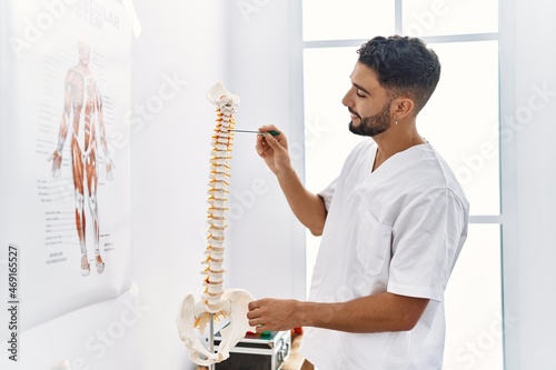 Young arab man wearing physiotherapist uniform pointing to vertebral column at clinic