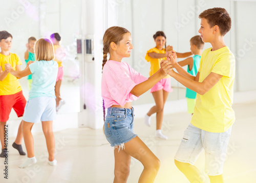 Portrait of happy modern tweenagers practicing active balroom dances in pairs in choreographic studio.