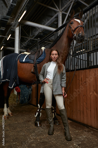 Portrait of smiling female jockey standing by horse in stable