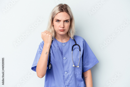 Young nurse woman isolated on blue background showing fist to camera, aggressive facial expression.