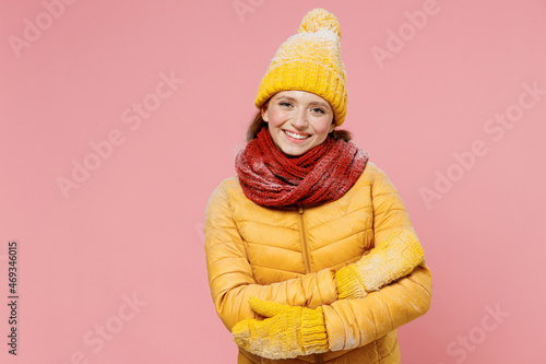 Businesslike smiling fascinating charismatic young woman 20s years old wears yellow jacket hat mittens looking camera hold hands crossed isolated on plain pastel light pink background studio portrait.
