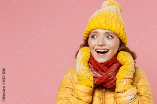 Impressed exultant young woman 20s wears yellow jacket hat mittens looking aside keep mouth open put hands on scarf wrapped around neck isolated on plain pastel light pink background studio portrait.