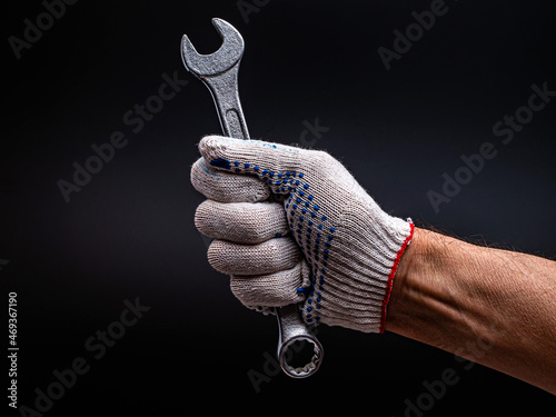 The right hand in a work glove holds a wrench on a dark background