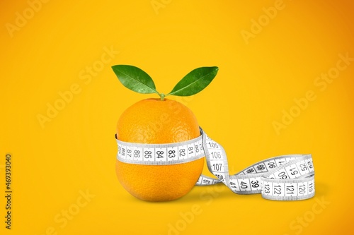 Fruit orange is wrapped with measuring tap as a symbol of cellulite on the skin.