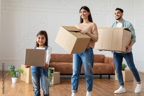 Happy young arab family carrying boxes in new flat