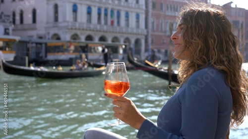 Girl holds in hand and drinks a glass of Spritz, in the city of love - aperitif, alcoholic drink Spritz Camapari or Aperol - typical drink of Venice made with white wine, orange - Rialto bridge 