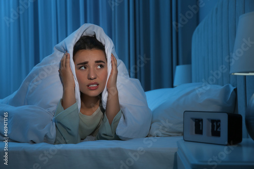 Unhappy young woman covering ears with blanket in bed at home. Noisy neighbours