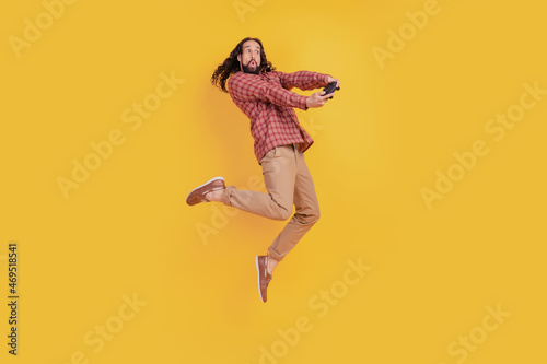 Photo of crazy addicted man jump hold controller wear checkered shirt isolated on yellow color background