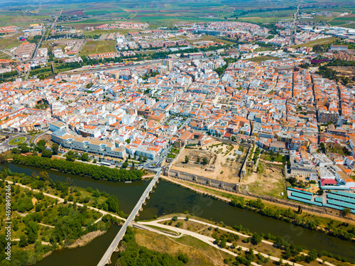 Aerial panoramic view of modern Merida cityscape on banks of Guadiana River with ancient pedestrian Roman Bridge, Spain