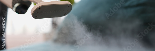 Cleaner washing green sofa with steamer at home closeup