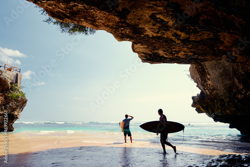 Hobby and vacation. Surfers with surfboard on beautiful beach with high rocks. Uluwatu spot, Bali island, Indonesia.